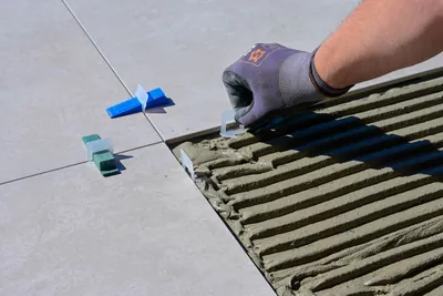A gloved hand aligning floor tiles using levelling spacers