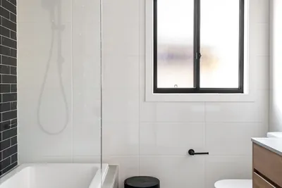 A bathroom finished in white marble tile with black accents and a freestanding tub